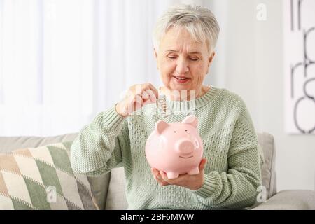 Ältere Frau, die zu Hause Geld in das Sparschwein legt Stockfoto