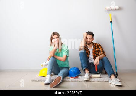 Müde junges Paar mit Werkzeugen sitzen in der Nähe von Lichtwand in der neuen Wohnung Stockfoto