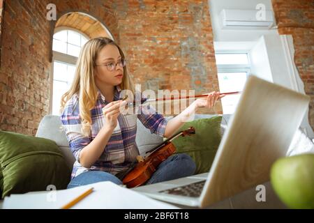 Junge Frau, die zu Hause während Online-Kursen oder kostenlose Informationen von sich aus studiert. Wird Musiker, Geiger, isoliert, Quarantäne gegen Coronavirus Verbreitung. Mit Laptop, Smartphone. Stockfoto