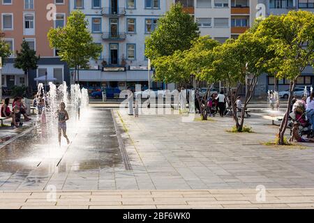 Kinder spielen in Wasserfontänen, während sich Einheimische auf Bänken im öffentlichen Bereich, Alter Messplatz, Mannheim, entspannen. Stockfoto