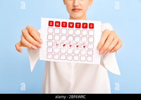 Junge Frau mit Kalender auf farbigem Hintergrund. Menstruationskonzept Stockfoto