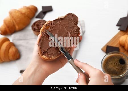 Frau, die Schokolade auf frisches Croissant verteilt, Nahaufnahme Stockfoto