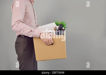 Arbeitslosigkeit. Entlassung. Entlassen Geschäftsmann verärgert mit einem Karton auf einem grauen Copyspace Hintergrund stehen. Arbeitslosenunterstützung. Stockfoto