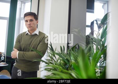Porträt von jungen selbstbewussten Geschäftsmann Blick auf Kamera, während im modernen Büro stehen Stockfoto