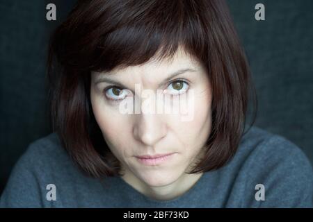 Frau schaut unter ihren Augenbrauen, runzelig und streng. Ein ernstes Gesicht aus nächster Nähe. Wut und Wariness Stockfoto
