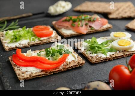 Knäckebrot mit schmackhaftem Frischkäse, Lachs, Eiern und Gemüse auf dunklem Hintergrund, Nahaufnahme Stockfoto