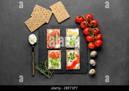Knäckebrot mit schmackhaftem Frischkäse, Lachs, Eiern und Gemüse auf dunklem Hintergrund Stockfoto
