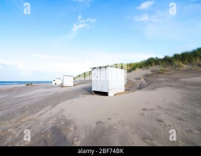 Kleines weißes Umkleiderhaus am Nordseestrand in den Niederlanden. Der blaue Himmel ist von Wolken durchsetzt. Stockfoto