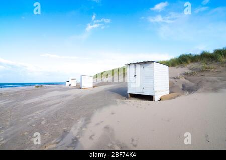 Kleines weißes Umkleiderhaus am Nordseestrand in den Niederlanden. Der blaue Himmel ist von Wolken durchsetzt. Stockfoto