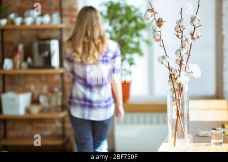 Porträt von wunderschönen Langhaar kaukasischen Frau zu Hause, gemütliche Atmosphäre, Fokus auf Blumen auf dem Tisch. Konzept des Arbeitens, Studierens zu Hause, häusliches Leben. Komfort, Quarantäne, Isolation. Stockfoto