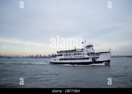 Ein Boot mit Touristen zur Freiheitsstatue. „Statue Cruises“. An einem bewölkten Tag voller Touristen. Stockfoto