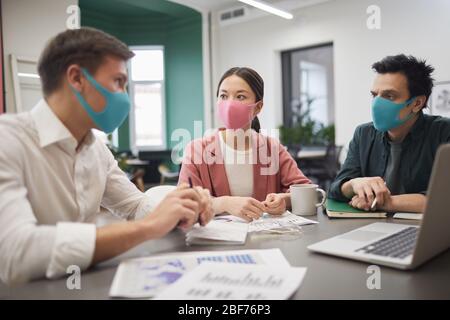 Eine Gruppe junger Geschäftsteams, die Schutzmasken tragen und diskutieren, arbeiten während des Meetings am Tisch zusammen Stockfoto