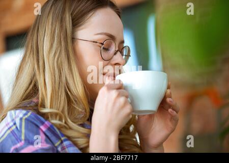 Nahaufnahme der schönen freudigen Frau Kaffee zu Hause trinken. Genießen Sie ihre Pause. Konzept des Arbeitens, Studierens zu Hause, häusliches Leben. Komfort, Quarantäne, Isolation. Aroma heißen leckeren Drink. Stockfoto