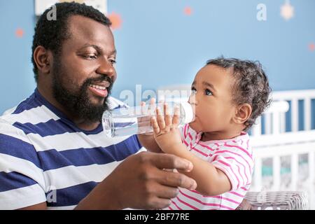 Afroamerikanischer Mann, der zu Hause Wasser für sein süßes Baby gibt Stockfoto