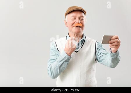 Portrait von älteren Mann mit Party-Dekor Selfie auf grauem Hintergrund Stockfoto