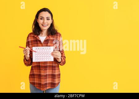 Junge Frau mit Menstruationskalender auf farbigem Hintergrund Stockfoto