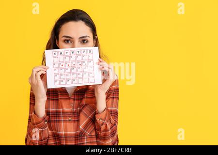 Junge Frau mit Menstruationskalender auf farbigem Hintergrund Stockfoto