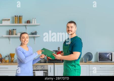 Schöner Klempner gibt Dokumente für junge Frau nach der Reparatur Waschbecken in der Küche Stockfoto