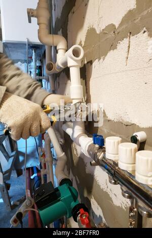 Installation der Heizung ein neues Haus, verbindet der Arbeiter das Rohr mit der Heizung des Kollektors.2020 Stockfoto