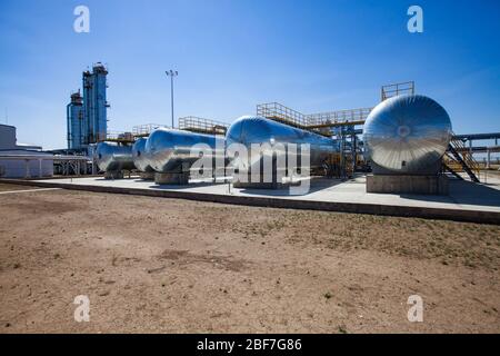 Ölraffinerie und Gasverarbeitungsanlage in der Wüste. Ein paar Wärmetauscher und Destillationstürme (Raffineriesäulen) auf blauem Himmel mit Sonne. Stockfoto