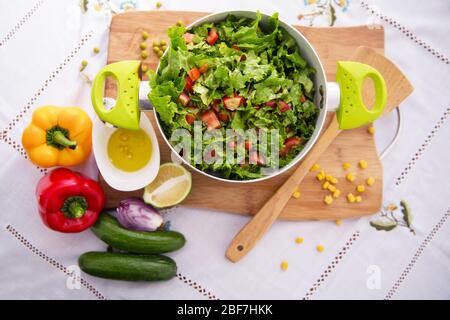 Oliven auf einer kleinen weißen Schüssel . Rote und orangefarbene Paprika. In Scheiben geschnittene grüne Zitrone. Holzlöffel. Gurken. Maiskörner . Pfeffer und Salat Salat Salat in einem grünen Stockfoto