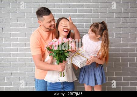 Ehemann und kleine Tochter grüßen Frau zum Muttertag auf grauem Backstein Hintergrund Stockfoto