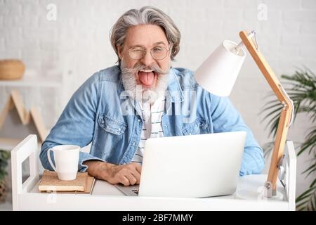 Glücklicher älterer Mann mit Laptop im Büro Stockfoto