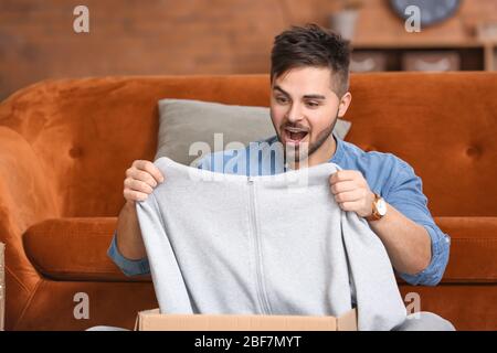Überraschte Mann Auspacken Box mit neuen Kleidern zu Hause Stockfoto