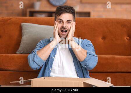 Überraschender Mann, der das Paket zu Hause auspacken kann Stockfoto