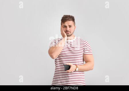 Trauriger Mann mit leerem Portemonnaie auf hellem Hintergrund Stockfoto