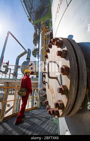 Region Aktobes/Kasachstan - Mai 04 2012: Ölraffinerieanlage. Techniker in roter Arbeitskleidung und gelber Helm auf Raffinierungssäule. CNPC-Unternehmen. Stockfoto