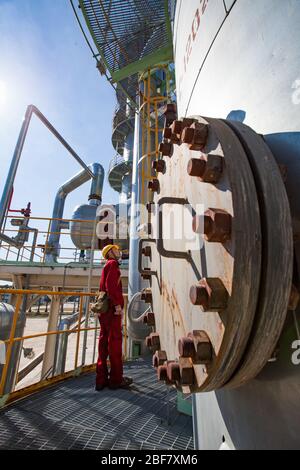 Region Aktobes/Kasachstan - Mai 04 2012: Ölraffinerieanlage. Techniker in roter Arbeitskleidung und gelber Helm auf Raffinierungssäule. CNPC-Unternehmen. Stockfoto