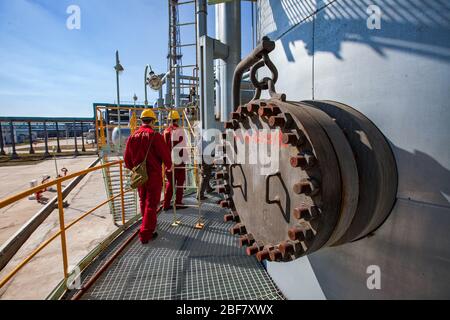 Region Aktobes/Kasachstan - Mai 04 2012: Ölraffinerieanlage. Zwei Wartungsarbeiter in roten Arbeitskleidung und gelbe Helme auf Raffinierungssäule. Auf Pipelin Stockfoto