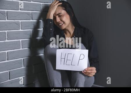 Erschrocken weiblichen Opfer hält Papierbogen mit Wort HILFE in der Nähe der Wand. Konzept der Gewalt Stockfoto