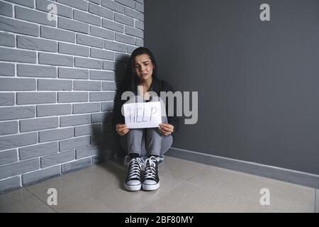 Erschrocken weiblichen Opfer hält Papierbogen mit Wort HILFE in der Nähe der Wand. Konzept der Gewalt Stockfoto