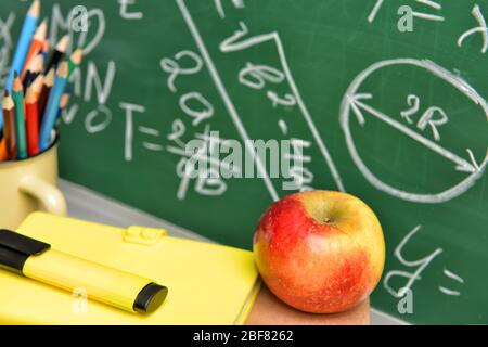 Set von Schulbedarf und Apfel auf dem Tisch in der Nähe Tafel Stockfoto