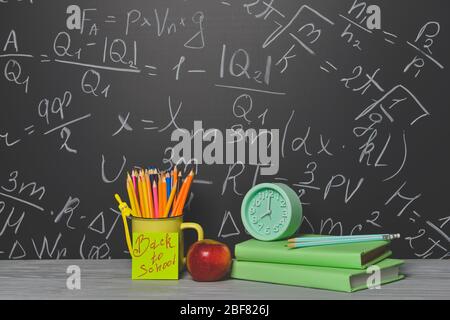 Set von Schulbedarf, Apfel und Uhr auf dem Tisch in der Nähe Tafel Stockfoto