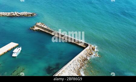 Ein einweisses Boot, das an einem sonnigen Tag am Meer festgemacht hat. Pier mit Zugang zum blauen Meer. Stockfoto