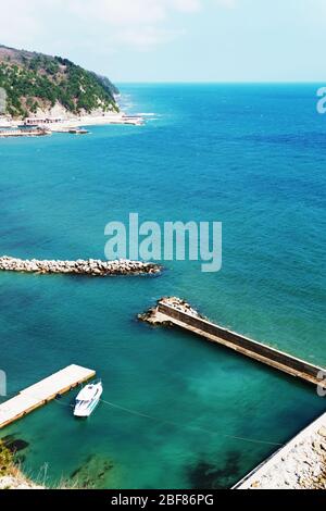 Ein einweisses Boot, das an einem sonnigen Tag am Meer festgemacht hat. Pier mit Zugang zum blauen Meer. Stockfoto