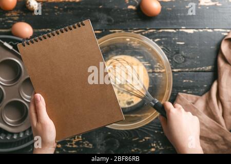Frau mit Kochbuch, die Teig am Tisch macht, Draufsicht Stockfoto