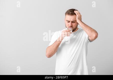 Junger Mann mit Glas Wasser, der an Kopfschmerzen auf hellem Hintergrund leidet Stockfoto