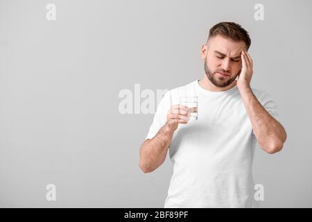 Junger Mann mit Glas Wasser, der an Kopfschmerzen auf hellem Hintergrund leidet Stockfoto