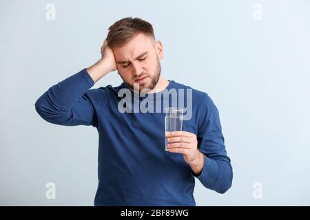 Junger Mann mit Glas Wasser, der an Kopfschmerzen auf hellem Hintergrund leidet Stockfoto