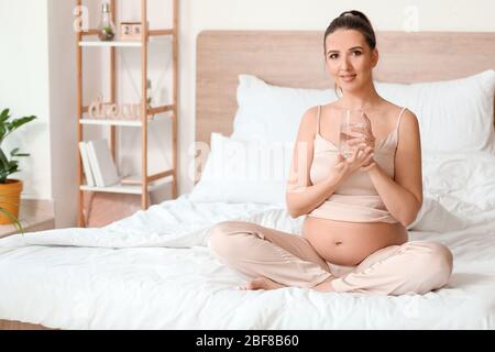 Schöne schwangere Frau Trinkwasser im Schlafzimmer Stockfoto