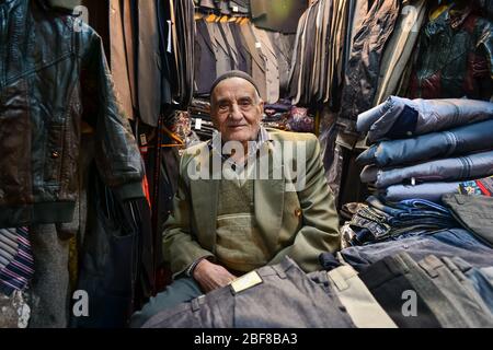 Tabriz, Iran - 22. November 2013: Iranischer Geschäftsmann verkauft Kleidung in einem kleinen überfüllten Laden im Bazar von Tabriz, einem alten Basar, der zum UNESCO-Weltkulturerbe gehört Stockfoto