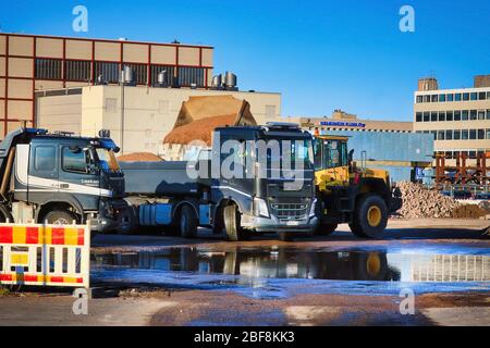 Komatsu Radlader Verladung Kies auf den Anhänger des schwarzen Volvo FH Kipper LKW auf der Baustelle an sonnigen Tag. Helsinki, Finnland. April 17, 2020 Stockfoto