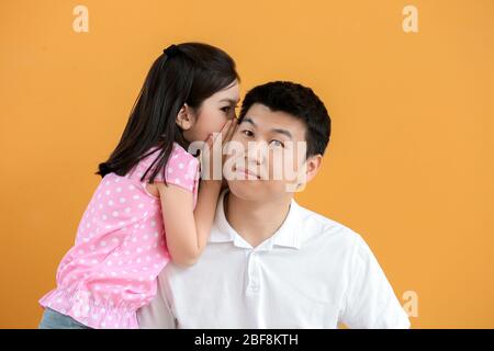 Kleine asiatische Mädchen erzählen Geheimnis zu ihrem Vater auf farbigen Hintergrund Stockfoto