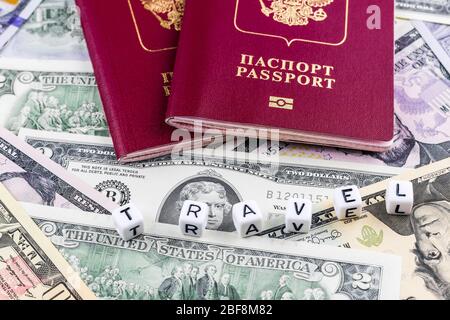 Zwei ausländische biometrische Pässe der Russischen Föderation vor dem Hintergrund von Dollarscheinen im Hintergrund und dem aus Würfeln angelegten Wort Reisen Stockfoto