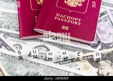 Zwei ausländische biometrische Pässe der Russischen Föderation vor dem Hintergrund von Dollarscheinen im Hintergrund und dem Wort Sommer aus Würfeln Stockfoto