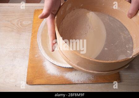 Große Schüssel, Schneidebrett, Sieb zum Sieben von Mehl auf dem Tisch. Weibliche Hände sieben Mehl in der Küche. Stockfoto